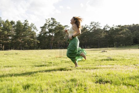 Einen Moment purer Freiheit eingefangen, rennt diese junge Frau freudig durch eine Wiese, ihr grüner Rock weht im sanften Sonnenuntergangslicht..