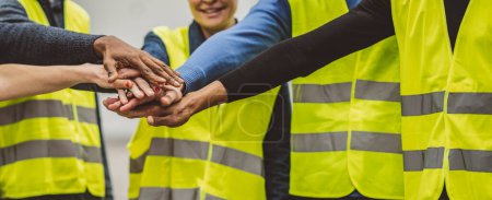 Close-up of diverse engineers stacking hands in a show of teamwork and unity in an industrial setting.
