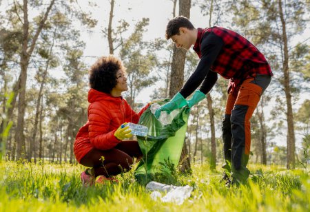 Deux jeunes adultes ramassant des déchets plastiques dans un parc forestier, promouvant la conservation de l'environnement et le travail d'équipe.