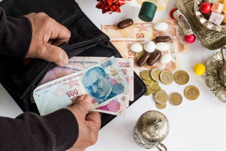 Téléchargez les photos : Turkish Banknotes in hand of older person on white with cologne,colorful candies and Turkish Coffee set.Feast bonus reflected in pensions concept - en image libre de droit