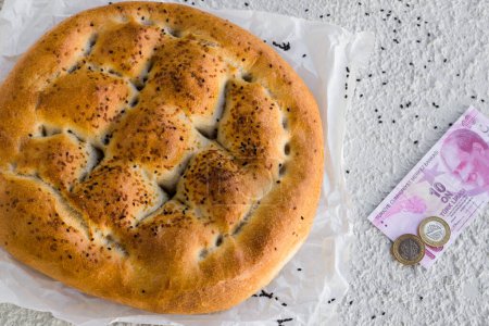 Téléchargez les photos : Pain de Ramadan turc traditionnel avec du papier cuisson à côté de douze lires sur un fond texturé blanc - en image libre de droit
