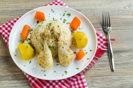 Téléchargez les photos : Jambes de poulet bouillies et légumes conçus sur une assiette blanche avec du riz beurré. - en image libre de droit