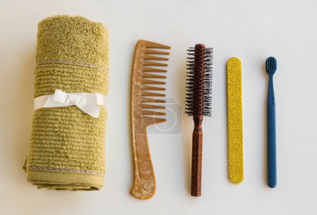 Téléchargez les photos : Une serviette propre et sèche, sur une surface blanche, conçue avec lime à ongles, peigne, brosse à dents et brosse à cheveux, vue de dessus. - en image libre de droit