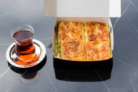 Téléchargez les photos : Patty au fromage tranché avec tasse de thé dans une boîte en carton sur une table en marbre - en image libre de droit
