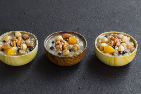 Téléchargez les photos : Dessert traditionnel turc Ashure ou Noah Puding, conçu dans des bols en bambou sur une surface noire - en image libre de droit