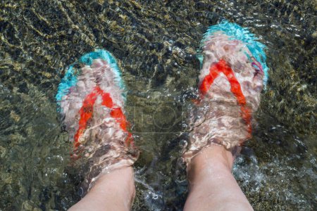 Téléchargez les photos : Pieds d'une femme inconnue, vêtue de tongs, dans l'eau, vue de dessus - en image libre de droit