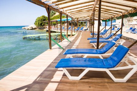 Téléchargez les photos : Des chaises longues blanches avec coussins bleus attendent leurs invités sur la jetée au bord de la mer. - en image libre de droit