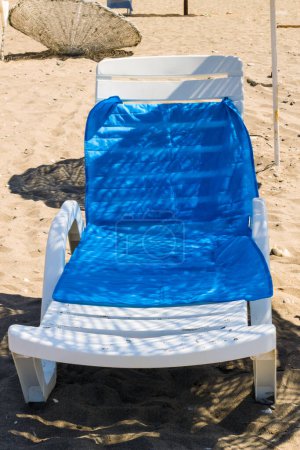 Téléchargez les photos : Chaise longue blanche vide avec serviette de mer bleue, sur la plage sous parapluie en paille - en image libre de droit