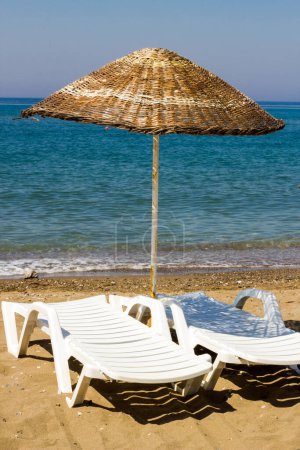 Téléchargez les photos : Calme et petite plage avec parasols en paille et chaises longues blanches vides sur le sable. Image conceptuelle de la saison estivale - en image libre de droit