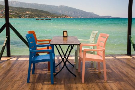Téléchargez les photos : Table vide avec quatre chaises colorées, sur la jetée au-dessus de la mer turquoise - en image libre de droit