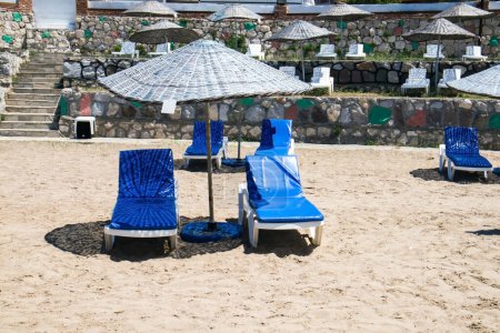 Téléchargez les photos : Calme et petite plage avec parasols en paille et chaises longues blanches vides sur le sable. Image conceptuelle de la saison estivale - en image libre de droit