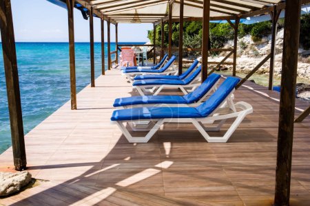 Téléchargez les photos : Des chaises longues blanches avec coussins bleus attendent leurs invités sur la jetée au bord de la mer. - en image libre de droit