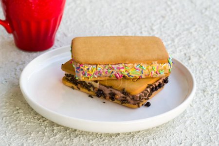 Téléchargez les photos : Sandwich crème glacée décorée avec des bonbons colorés est conçu dans une assiette blanche. - en image libre de droit