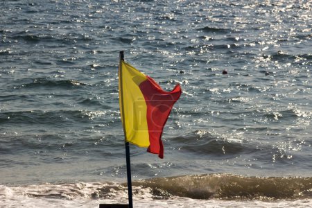 Foto de Bandera amarilla y roja ondeando por el fuerte viento, advirtiendo que el mar es peligroso - Imagen libre de derechos