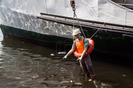 Téléchargez les photos : Mannequin homme sans vie en gilet de sauvetage et bouée de sauvetage suspendue par des cordes du navire au-dessus de la mer - en image libre de droit