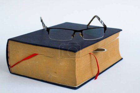 Téléchargez les photos : Ancien livre à couverture rigide sur surface blanche avec lunettes de lecture et signet, concept éducatif - en image libre de droit