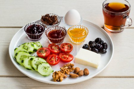 Téléchargez les photos : Assiette de petit déjeuner blanche avec tomates cerises tranchées, concombre et oeuf bouilli avec tasse à thé sur table en bois - en image libre de droit