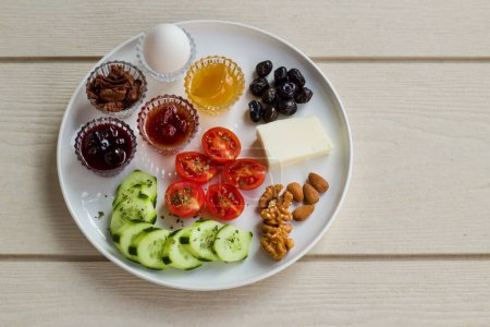 Téléchargez les photos : Assiette de petit déjeuner blanche avec tomates cerises tranchées, concombre et oeuf bouilli avec espace de copie sur la table en bois. - en image libre de droit