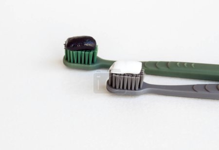 Téléchargez les photos : Deux brosses à dents avec charbon noir et dentifrice fluorure sur une surface blanche avec espace de copie - en image libre de droit