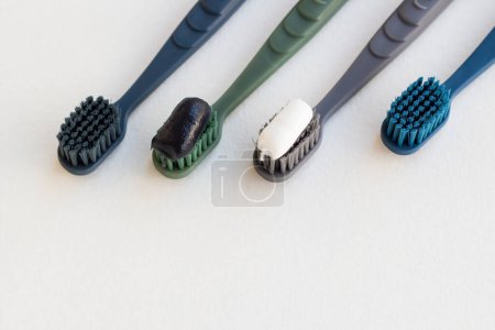 Téléchargez les photos : Quatre brosses à dents avec charbon de bois noir et dentifrice fluorure sur surface blanche - en image libre de droit