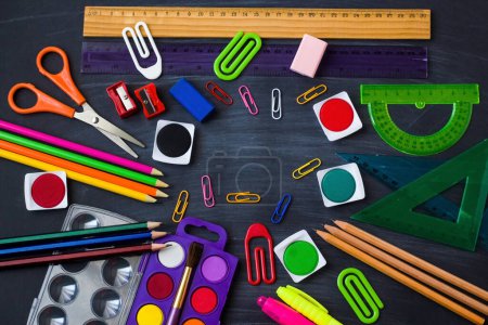 Téléchargez les photos : L'école colorée fournit ensemble aquarelle, crayons et crayons sur fond noir poussiéreux de craie. - en image libre de droit