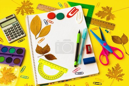 Téléchargez les photos : Fournitures scolaires colorées avec des feuilles d'automne sèches sur un fond jaune - en image libre de droit