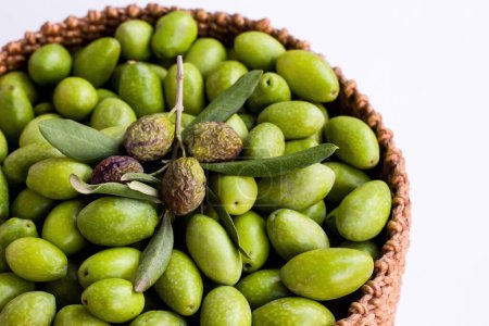 Téléchargez les photos : Olives naturelles vertes fraîchement récoltées dans un panier en osier sur une surface blanche - en image libre de droit