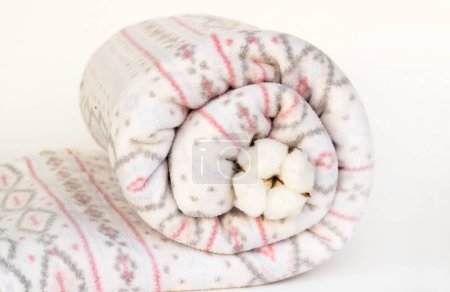 Téléchargez les photos : Couverture en laine douce, molleton enroulé dans un tourbillon avec une poupée en coton naturel sur la surface blanche - en image libre de droit