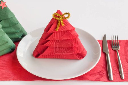 Téléchargez les photos : Couleur rouge, serviette en papier pliée en forme d'arbre de Noël sur plaque blanche avec ensemble de couverts - en image libre de droit