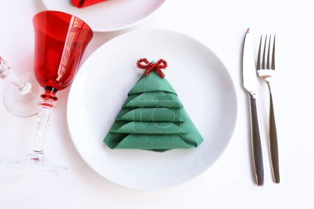 Téléchargez les photos : Serviette en papier verte pliée en forme de pin sur une assiette avec couverts ensemble verre de champagne rouge - en image libre de droit