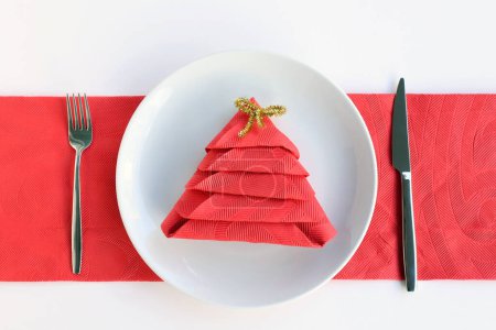 Téléchargez les photos : Serviette rouge pliée en forme de pin dans une assiette avec couverts Concept de Noël ou Nouvel An - en image libre de droit