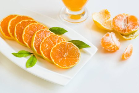 Téléchargez les photos : Mandarine fraîche, ronde, coupée en tranches avec des feuilles vertes fraîches, conçue sur une assiette blanche - en image libre de droit