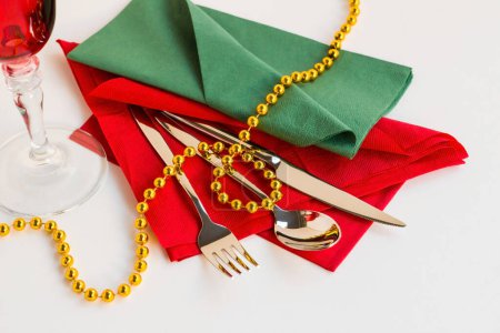 Téléchargez les photos : Serviettes de Noël de couleur rouge et verte pliées sur une surface blanche avec ensemble de couverts et chaîne de Noël en or - en image libre de droit