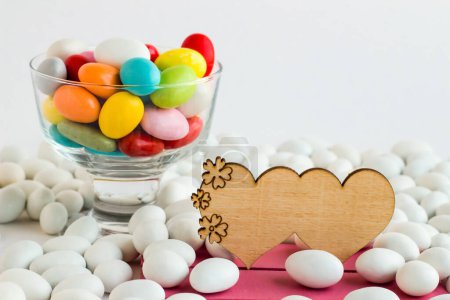Téléchargez les photos : Bol à bonbons aux amandes colorées conçu avec un cœur blanc en bois sur une surface blanche.Image conceptuelle - en image libre de droit