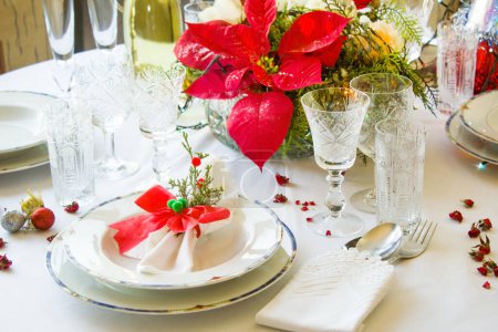 Téléchargez les photos : Mise en place d'une table à manger de Noël avec des serviettes en tissu, ensemble de dîner en porcelaine blanche chic, verres en cristal et fleur de poison rouge - en image libre de droit