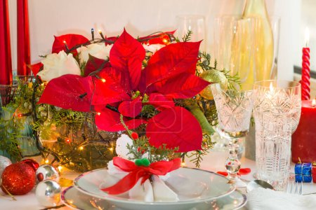Téléchargez les photos : Mise en place d'une table à manger de Noël avec des serviettes en tissu, ensemble de dîner en porcelaine blanche chic, verres en cristal et fleur de poison rouge - en image libre de droit
