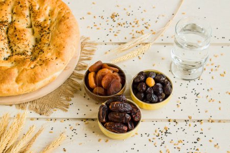 Téléchargez les photos : Farine d'iftar, temps de rompre avec des dattes sucrées et sèches, abricot, olives noires, eau et pain Ramadan sur la planche de bois.. - en image libre de droit