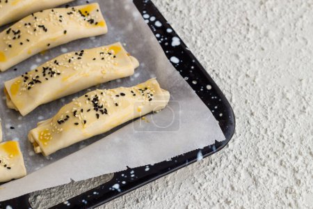 Téléchargez les photos : Croustillant, fromage et olives enveloppés dans la farce, brossé avec du jaune d'oeuf, prêt à cuire sur du papier cuisson sur une plaque à pâtisserie. - en image libre de droit