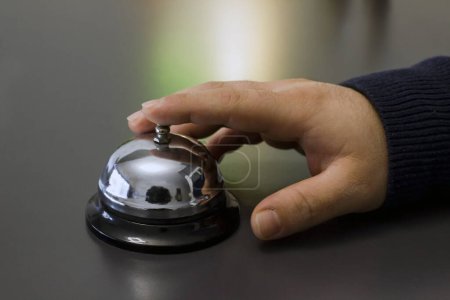 Téléchargez les photos : Gros plan d'une main en utilisant une cloche de réception d'hôtel en métal gris - en image libre de droit