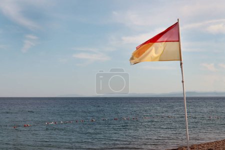 Téléchargez les photos : Drapeau d'avertissement aux couleurs jaune et rouge agitant dans le vent sur le bord de mer ou la plage - en image libre de droit