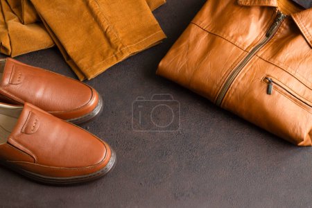 Téléchargez les photos : Cuir véritable, chaussures pour hommes, manteaux et pantalons en cuir pliés sur une surface sombre avec espace de copie - en image libre de droit