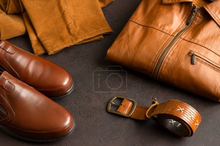 Foto de Cuero genuino, zapatos de hombre, abrigos de cuero plegados y pantalones en superficie oscura con cinturón de cuero - Imagen libre de derechos