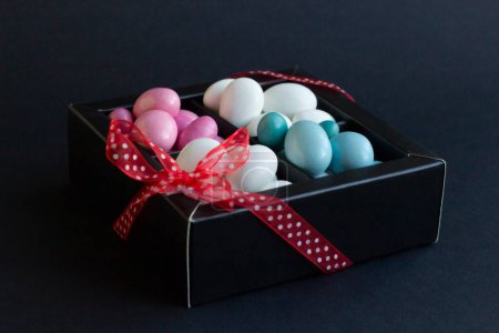 Téléchargez les photos : Bonbons aux amandes traditionnels, blancs et pastel colorés, recouverts de chocolat en boîte noire avec ruban rouge - en image libre de droit