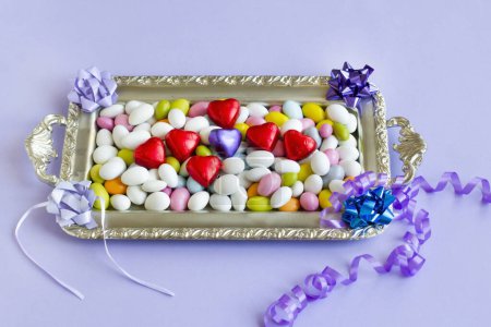 Téléchargez les photos : Des bonbons aux amandes colorées ont été conçus sur un plateau en argent avec des chocolats enveloppés en forme de cœur. - en image libre de droit