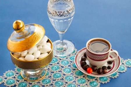 Téléchargez les photos : Traditionnel turc dur, bonbons aux amandes conçus sur une surface bleue avec du café, de l'eau et des tissus en dentelle faits à la main. - en image libre de droit