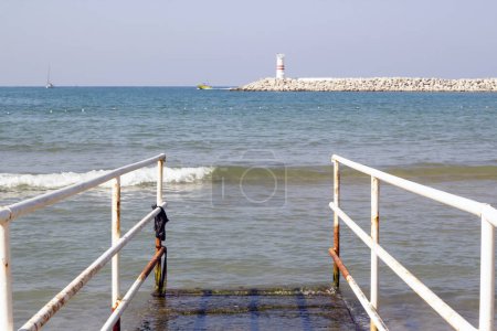 Téléchargez les photos : En bord de mer, rampe inclinée pour handicapés, avec phare - en image libre de droit