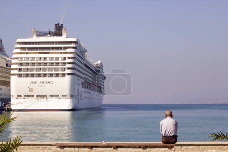 Téléchargez les photos : Kusadasi-Aydin-Turquie 10.17.2023 Un inconnu est assis sur la plage, regardant le bateau de croisière - en image libre de droit