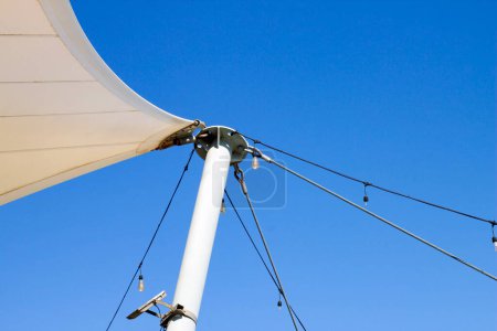 White tarpaulin canopy, stretched with steel wires, in the blue sky