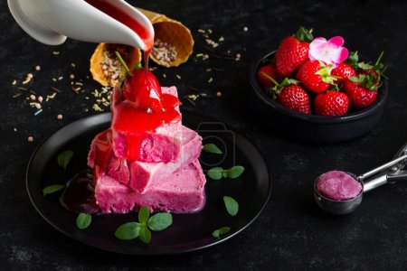 Téléchargez les photos : Crème glacée aux fraises, conçue sur une assiette ronde noire, sauce aux fraises coulant du bol à sauce - en image libre de droit