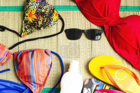 Téléchargez les photos : Haut de bikini coloré, conçu sur une surface en osier, avec des lunettes de soleil et de l'huile de soleil - en image libre de droit
